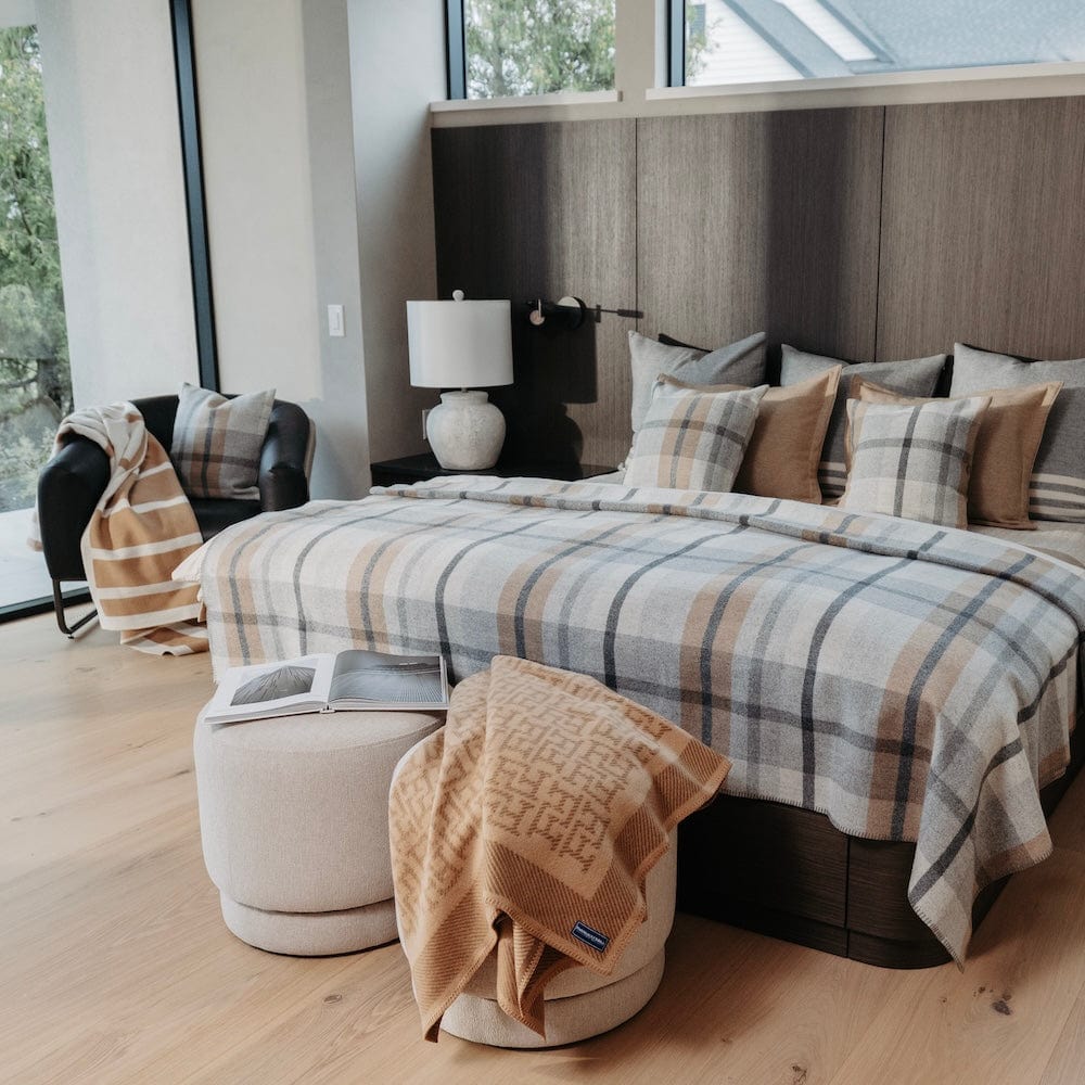 Northfield Plaid Heritage Beige heavyweight wool blanket on a bed, styled with camel and plaid pillows, a matching throw, and a modern headboard.