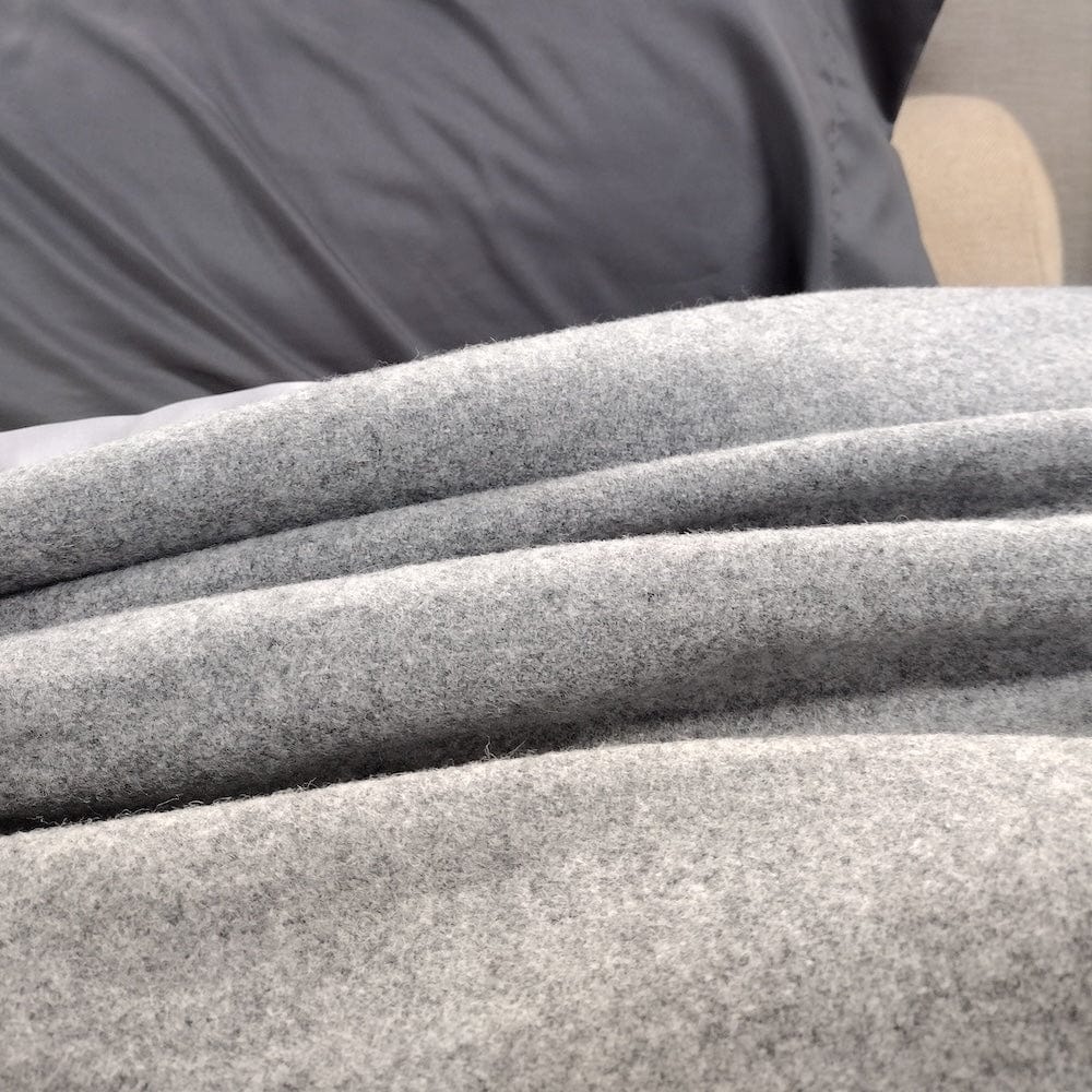 Pure and Simple Heather Gray middleweight wool blanket in a textured close-up on a bed, layered next to a smooth, dark grey pillow.