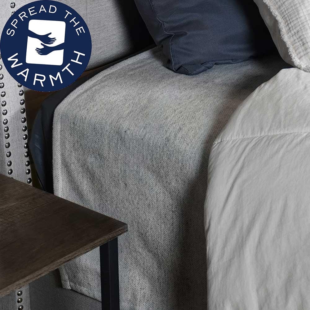 Lakefront Natural lightweight wool blanket draped over the corner of a modern bed with a studded headboard and dark wood side table in a lifestyle setting.
