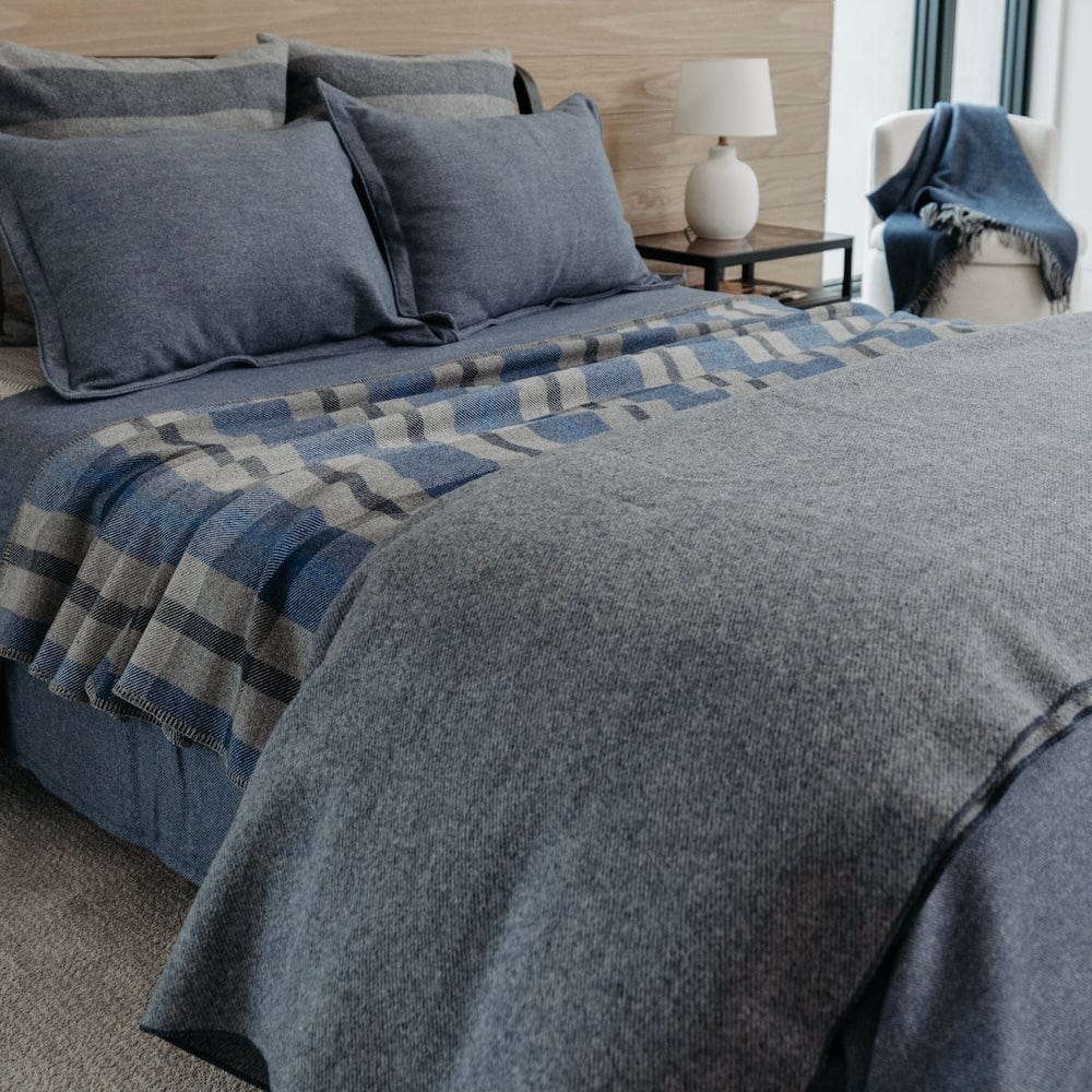 Summit Navy heavyweight wool blanket folded on a bed, styled with matching navy pillows and a coordinating blue and grey plaid throw blanket.