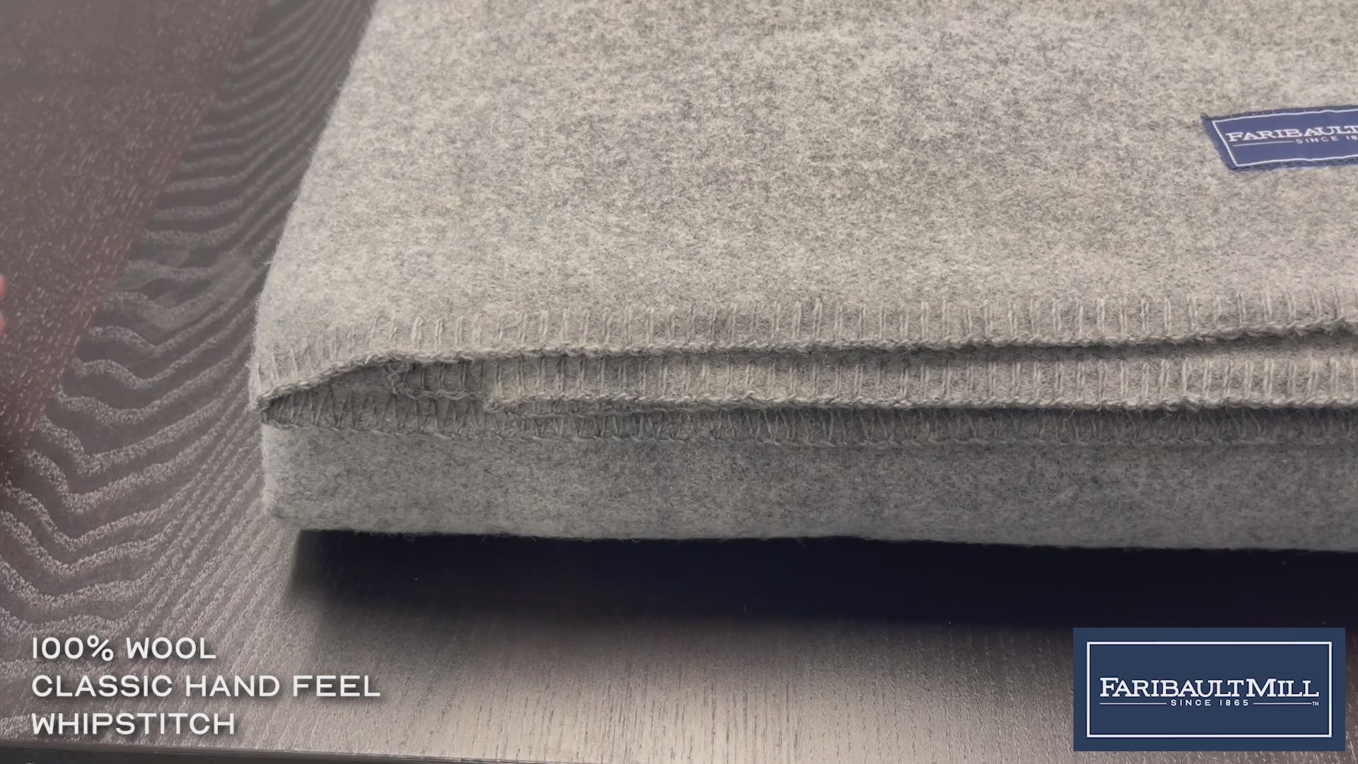 Close-up video of a hand feeling the soft, lofted texture and whipstitched edge of the heather gray Pure and Simple wool blanket.