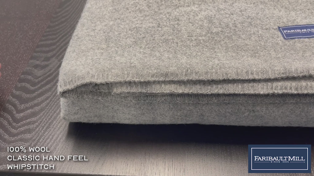 Close-up video of a hand feeling the soft, lofted texture and whipstitched edge of the heather gray Pure and Simple wool blanket.