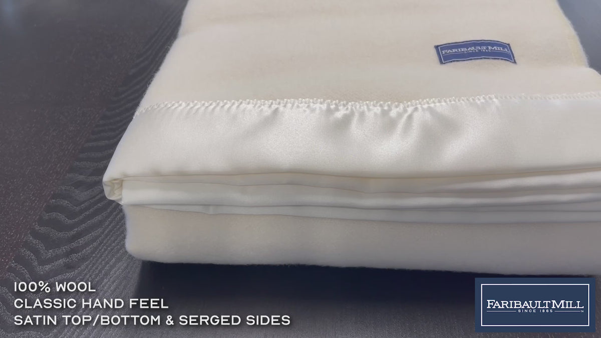 Close-up video of a hand feeling the soft, lofted texture and whipstitched edge of the heather gray Pure and Simple wool blanket.