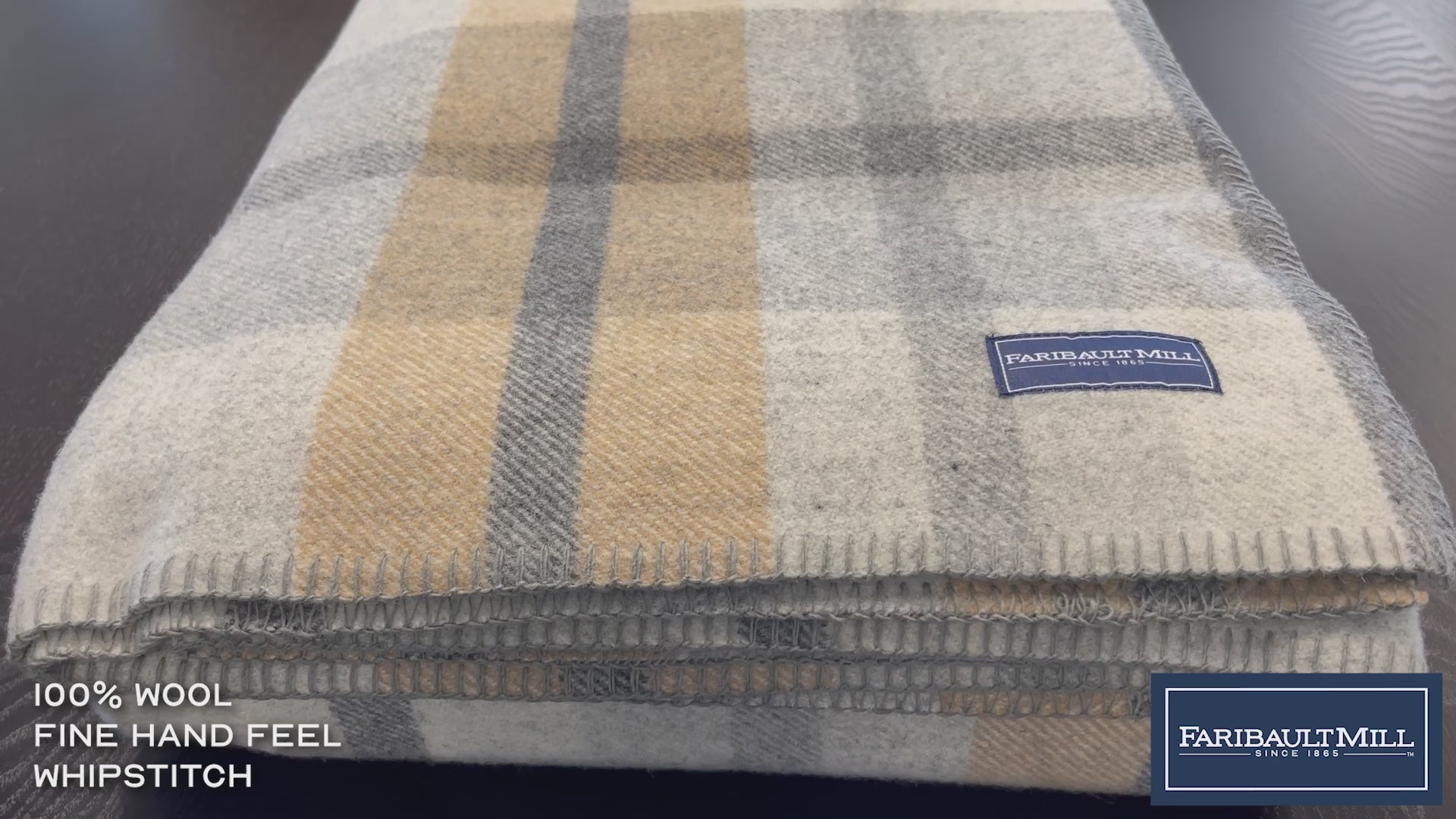 Close-up video of a hand feeling the soft, lofted texture and whipstitched edge of the heritage beige Northfield Plaid wool blanket.
