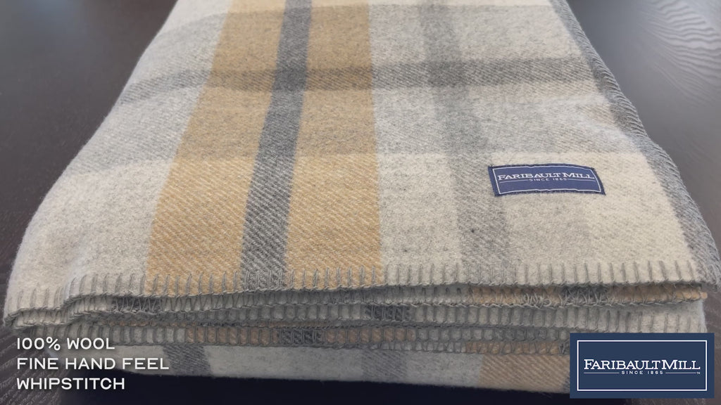 Close-up video of a hand feeling the soft, lofted texture and whipstitched edge of the heritage beige Northfield Plaid wool blanket.