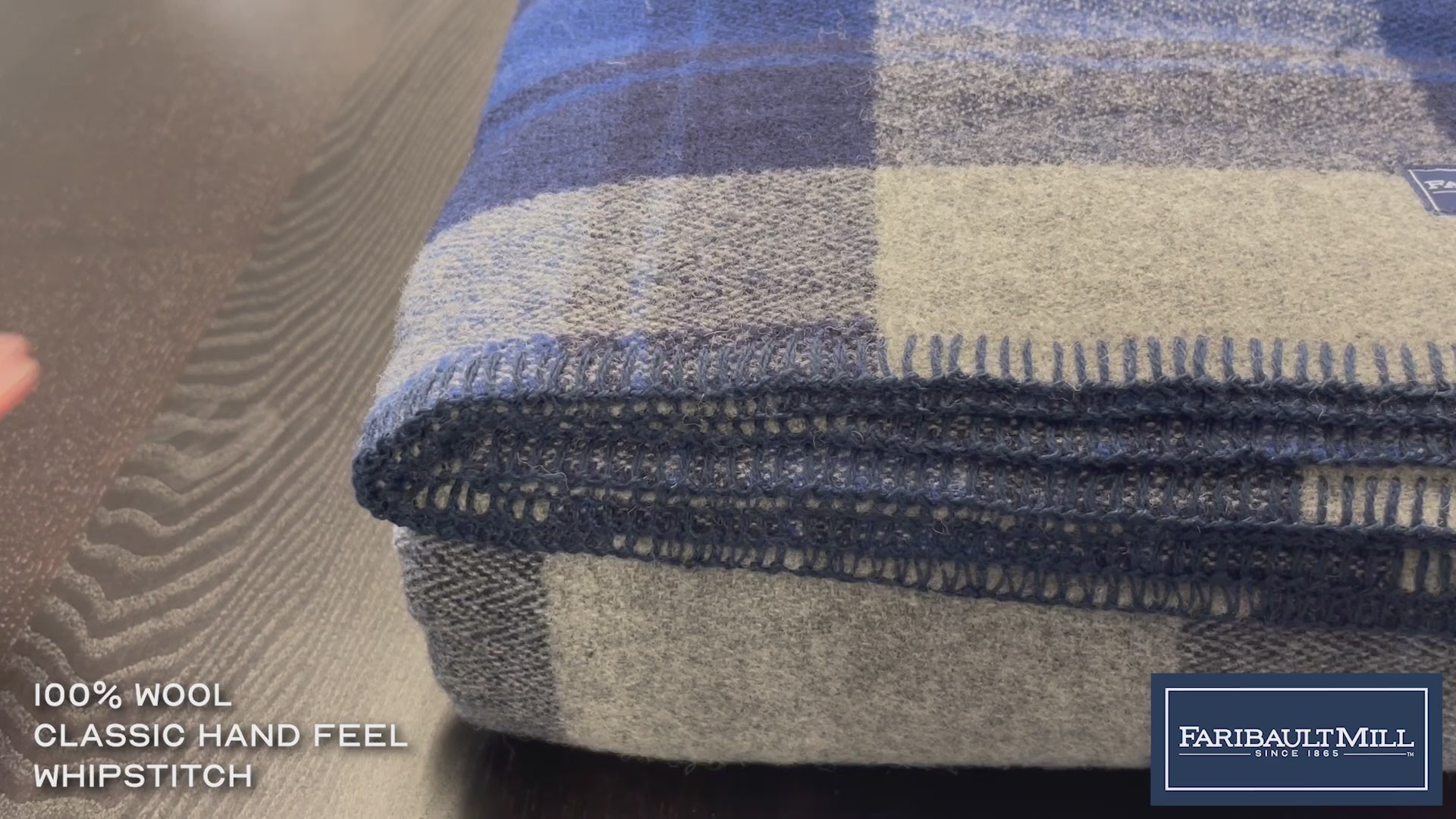 Close-up video of a hand feeling the soft, lofted texture and whipstitched edge of the blue North Shore wool blanket.